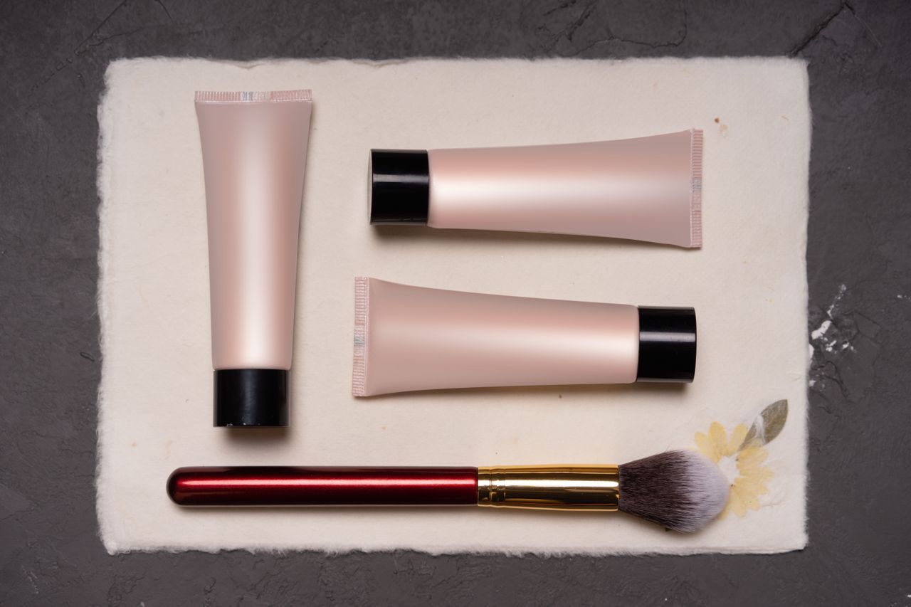 services-01 Beauty composition featuring cosmetic tubes and a makeup brush on a textured background.
