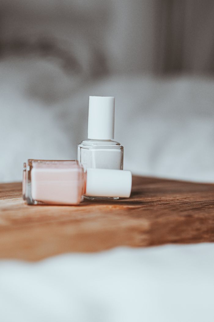 embark Close-up of pink and white nail polish bottles on a wooden tray with a blurred background.