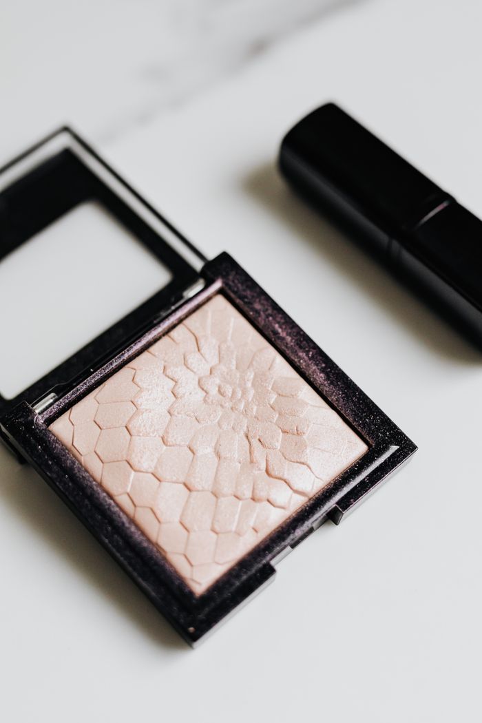 our-story Flat lay of a textured highlighter compact and lipstick on a white surface, perfect for beauty and cosmetic themes.