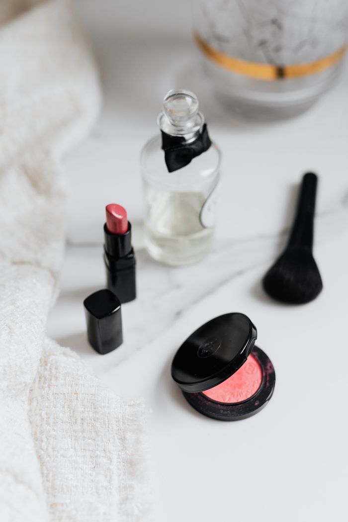 gallery-04 A flat lay of beauty products including lipstick, blush, and a perfume bottle on a marble surface.