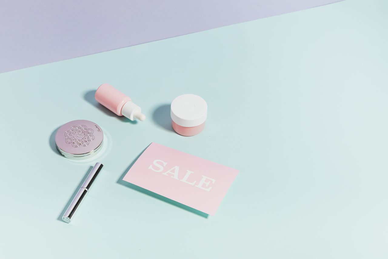 gallery-02 Clean flat lay of pastel pink beauty products and sale card on a light background.